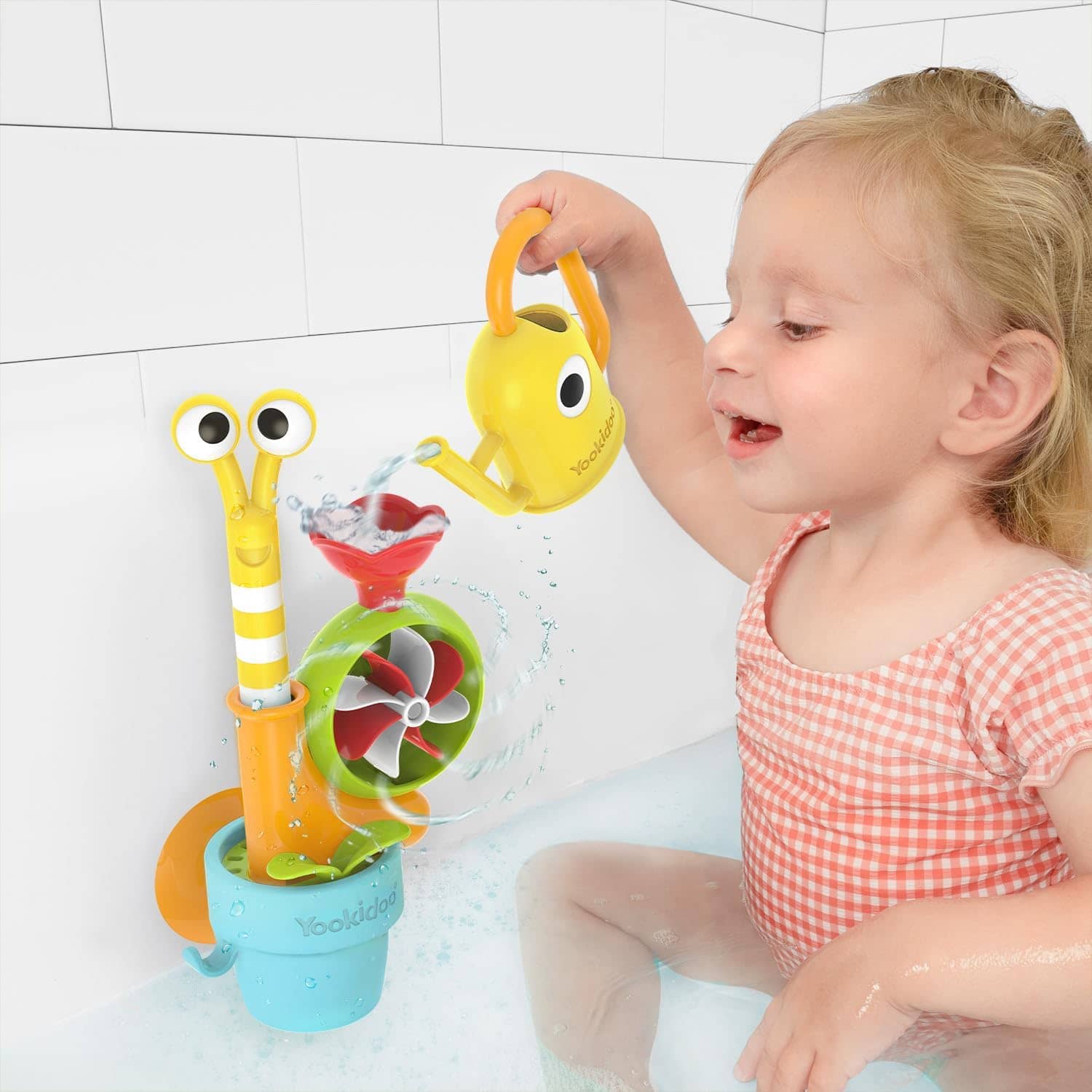 Kind spielt mit buntem Badespielzeug in der Badewanne und gießt Wasser mit Gießkanne