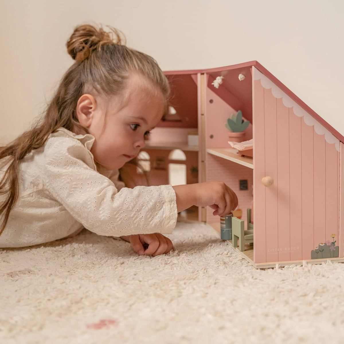 Spielzeug ab 3 Jahren mit Mädchen, das ein rosa Puppenhaus auf einem Teppich spielt
