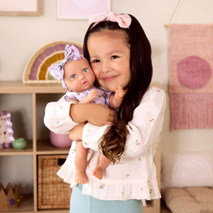 Babypuppe mit Schnuller – in einem Kleidchen mit Blümchenmuster und einem Haarband