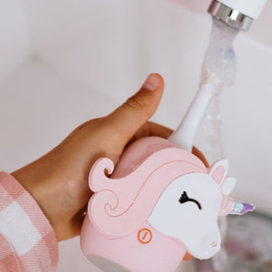 Kinderhand hält die Einhorn-Schallzahnbürste unter den Wasserhahn