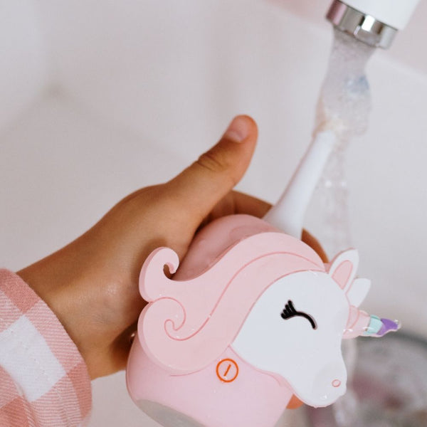 Kinderhand hält die Einhorn-Schallzahnbürste unter den Wasserhahn