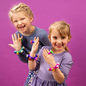 Zwei Mädchen tragen bunte Armbänder und Ringe aus dem Schmuckset Plip Charms – Türkis von Fat Brain Toys