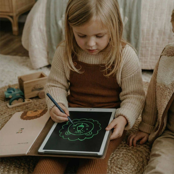Kind malt mit einem Grafiktablett für Kinder auf einer weichen Unterlage neben einem Spielzeugauto