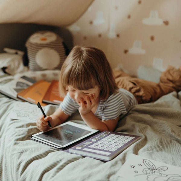 Kind, das auf einem Bett mit dem Grafiktablett Kidydraw Mini – Es war einmal vor langer Zeit zeichnet
