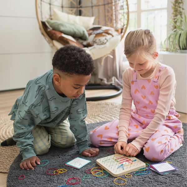 Kinder spielen mit einem BS Toys Holz Geoboard für Kinder und bunten Gummibändern auf einem Teppich