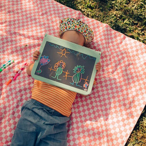 Kind zeichnet mit der Leuchttafel Kidydraw Pro auf einer Picknickdecke im Freien