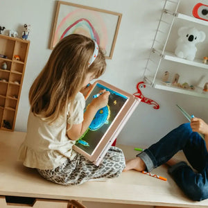 Mädchen zeichnet mit Leuchttafel Kidydraw Pro in einem kreativen Kinderzimmer, farbenfrohe Kunstwerke