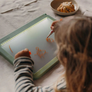 Kind, das mit dem Leuchttafel Kidydraw Pro orangefarbene Zeichnungen macht.