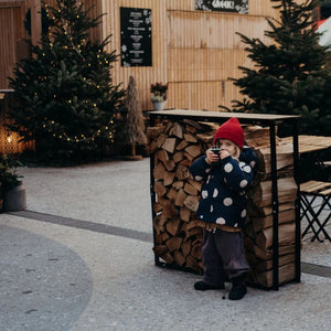Kind mit Walkie-Talkie Set, das hinter einem Holzstapel steht, umgeben von Weihnachtsdekoration