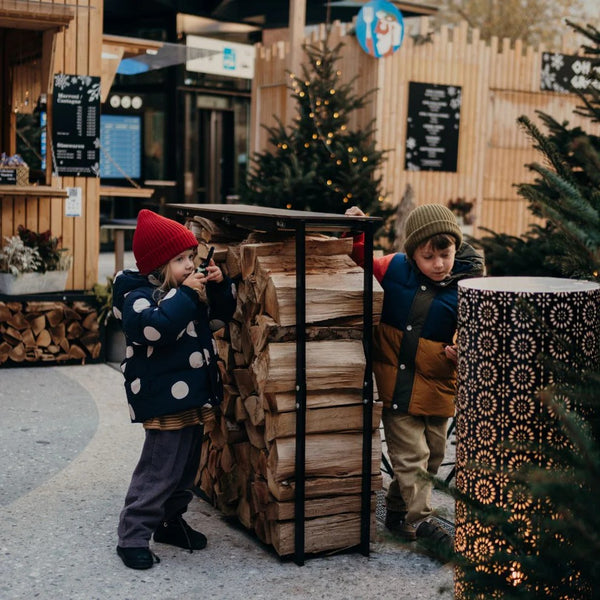Zwei Kinder, die mit einem Walkie-Talkie Set im Freien spielen, umgeben von Holz und festlicher Dekoration.