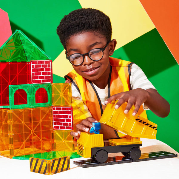 Ein Junge im Sicherheitshemd spielt mit Magnetbausteinen für Kinder und baut ein buntes Haus
