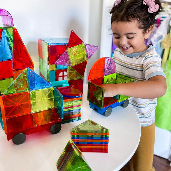 Ein Kind spielt mit bunten Magnetbausteinen Kinder von MAGNA-TILES auf einem Tisch