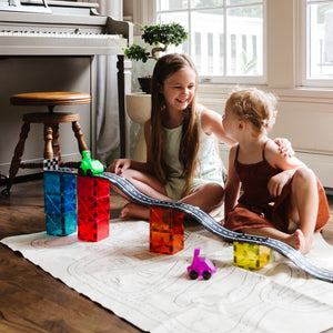 Zwei Kinder spielen mit Magnetbausteinen Kinder und einer Rennstrecke aus MAGNA-TILES im Wohnzimmer