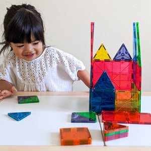 Ein Kind spielt mit MAGNA-TILES Magnetbausteine Kinder und baut bunte Strukturen auf einem Tisch