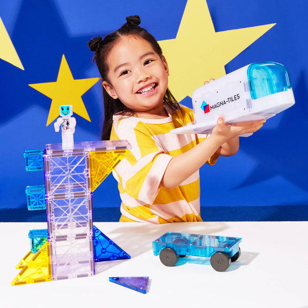 Ein Mädchen spielt mit MAGNA-TILES Magnetbausteine Kosmos Set und einem blauen Auto