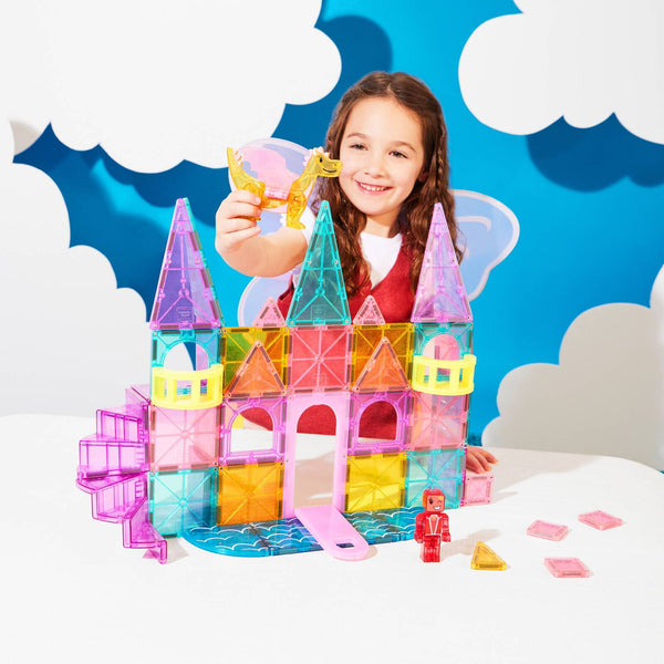 Mädchen spielt mit Magnetbausteine Schloss Set und präsentiert ein pinkes Element vor einem bunten Hintergrund