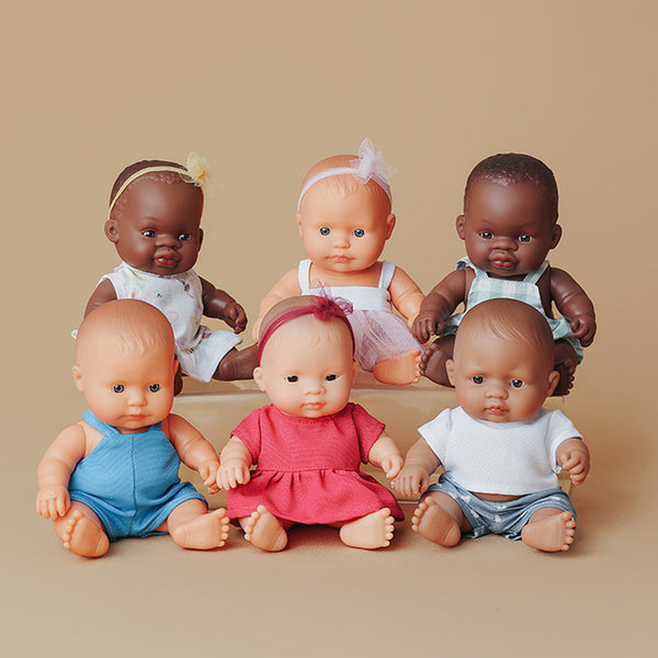 Sechs Miniland Puppen unterschiedlicher Hauttöne und Kleidung, sitzend vor beigem Hintergrund