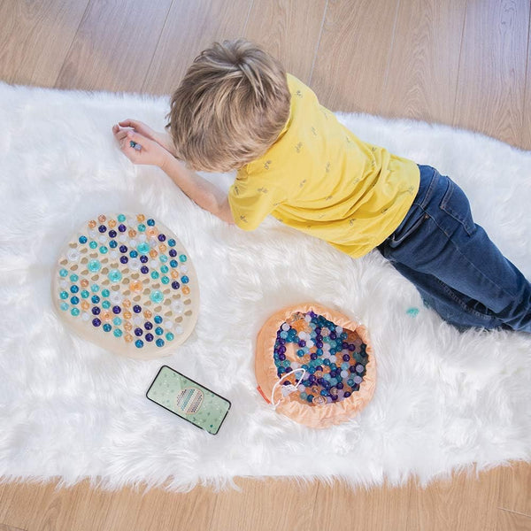 Kind spielt mit dem bunten Puzzle – Mandala-Stein von Miniland auf weißem Teppich