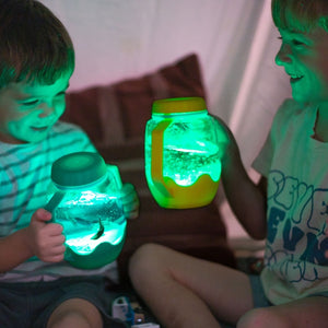 Zwei Kinder spielen mit dem Glo Pals Sensorik-Glas zum Befüllen mit Wasser – grün in dunkler Umgebung