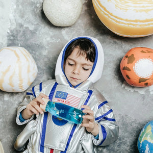Ein Kind in Astronautenkleidung untersucht eine Sensorikflasche für Kinder auf dem Boden mit Planeten.