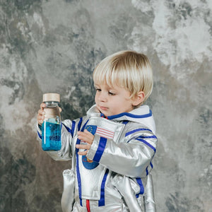 Kleines Kind im Raumanzug mit einer Sensorikflasche für Kinder in der Hand, die glitzernde Flüssigkeit enthält