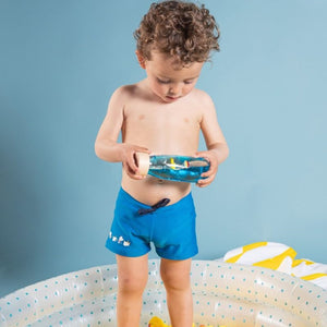 Kleiner Junge mit blauen Shorts spielt mit einer Sensorikflasche für Kinder im Wasserbecken