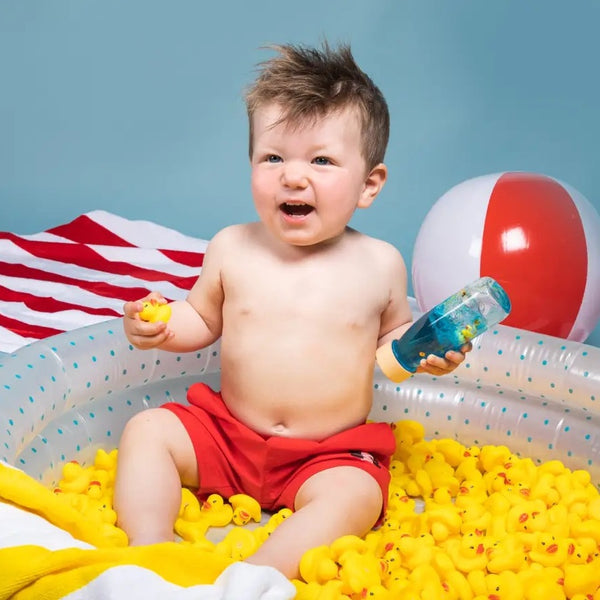 Glückliches Kind mit Sensorikflasche für Kinder im Schwimmbecken voller gelber Enten