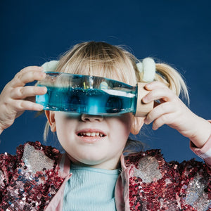 Kind mit Sensorikflasche für Kinder, die mit blauen Flüssigkeiten und Spielzeug gefüllt ist
