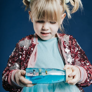 Mädchen mit funkelndem Jacket hält eine Sensorikflasche für Kinder mit bunten Figuren und Wasser